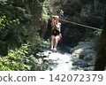 Adventurous Woman Ziplining Over Scenic River Gorge 142072379