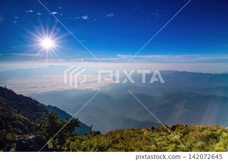 sunshine in colorful blue sky over village of hills scene from top of mountain high ground with some silhouette shade and wave of fog and mist below sunshine in colorful blue sky over village of hills scene from top of mountain high ground with some silhouette shade and wave of fog and mist below 142072645