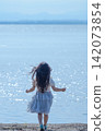 [Vertical, Wide Shot] A girl in a white dress walks along a lakeside shimmering in the backlight | Her hair blowing in the wind, seen from behind. 142073854