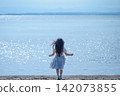 [Horizontal] A girl in a white dress walks along the lakeside, shimmering in the backlight | Her hair blowing in the wind, seen from behind. 142073855