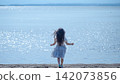 [Horizontal, Wide] A girl in a white dress walks along the lakeside, sparkling in the backlight | Her hair blowing in the wind, seen from behind. 142073856