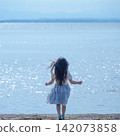 [Square] A girl in a white dress walks along a lakeside shimmering in the backlight | Her hair blowing in the wind, seen from behind. 142073858