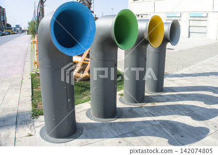 Four colour coded funnel shaped waste bins in a row on a sunlit pavement Four colour coded funnel shaped waste bins in a row on a sunlit pavement 142074805