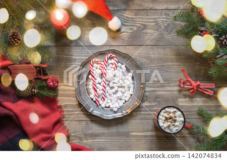 Christmas composition of plate with sweets, cup of coffee, wreath, checkered pleid on wooden board. Flat lay. Top view. Copy space. Christmas composition of plate with sweets, cup of coffee, wreath, checkered pleid on wooden board. Flat lay. Top view. Copy space. 142074834