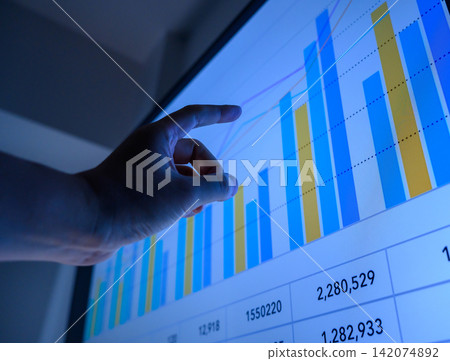 A business person points to a graph on a monitor to conduct market analysis. 142074892