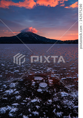A breathtaking view of the sky painted in the colors of the sunrise, frost flowers spreading across the frozen ice of Lake Akan, and Mount Oakan. A breathtaking view of the sky painted in the colors of the sunrise, frost flowers spreading across the frozen ice of Lake Akan, and Mount Oakan. 142075290