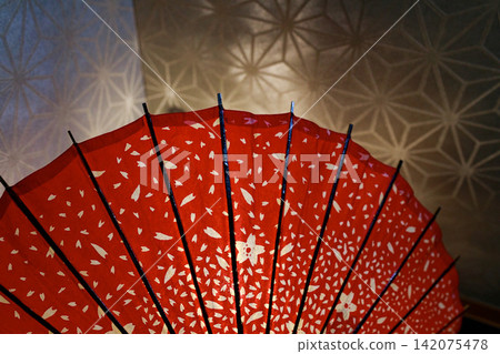 A red Japanese umbrella adorned with cherry blossom patterns and a Japanese-style lighting display. A red Japanese umbrella adorned with cherry blossom patterns and a Japanese-style lighting display. 142075478