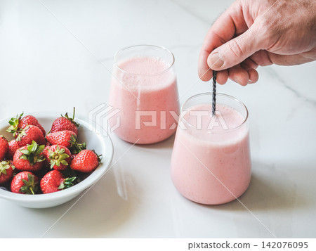 Hands stirring strawberry yogurt with a spoon Hands stirring strawberry yogurt with a spoon 142076095