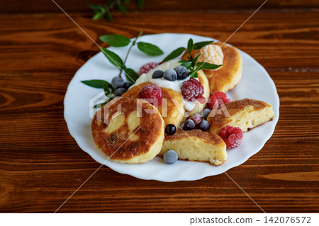 Cottage cheese pancakes with berries on brown wooden background Cottage cheese pancakes with berries on brown wooden background 142076572