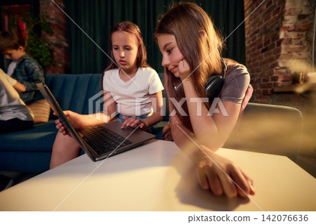 Older girl guiding younger girl while they use laptop together at home 142076636