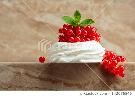 Pavlova dessert with red currant and mint on a beige table. Pavlova dessert with red currant and mint on a beige table. 142076846