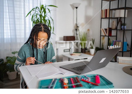 Girl completing homework at desk with laptop for remote learning Girl completing homework at desk with laptop for remote learning 142077033