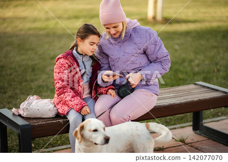 Mother daughter looking at smartphone caring for dog Mother daughter looking at smartphone caring for dog 142077070