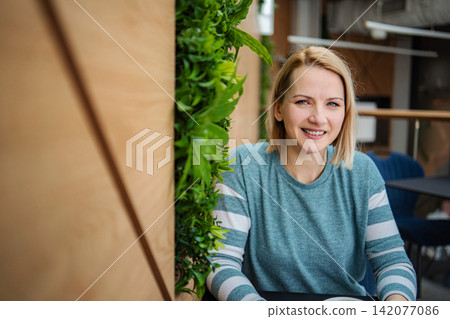 Blonde woman smiling in a modern cafe with green wall Blonde woman smiling in a modern cafe with green wall 142077086