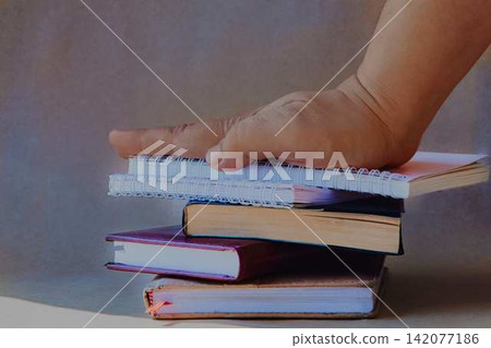 Notebooks and organizers on a light sandy background in bright light with a person's hand on top of them. Notebooks and organizers on a light sandy background in bright light with a person's hand on top of them. 142077186