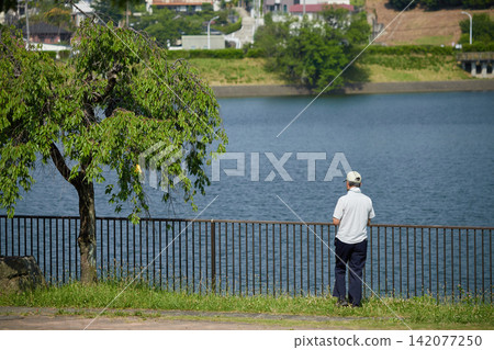 一位老人在夏日公園的池塘邊散步。 一位老人在夏日公園的池塘邊散步。 142077250