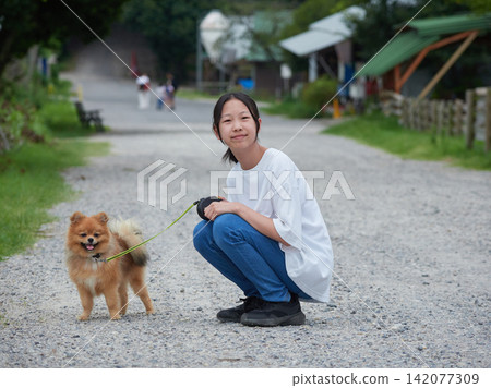 A middle school girl on summer vacation is seen walking a cute Pomeranian puppy in a pasture in the middle of summer. A middle school girl on summer vacation is seen walking a cute Pomeranian puppy in a pasture in the middle of summer. 142077309