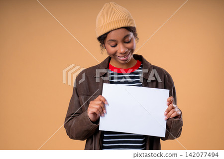 Smiling Pretty Teenage Girl Holding Horizontal Blank White A4 Paper Poster Toward Camera, Young Smiling Pretty Teenage Girl Holding Horizontal Blank White A4 Paper Poster Toward Camera, Young 142077494