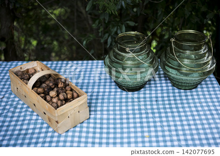 Autumn picnic with walnuts in a wooden basket with glass lanterns on a checkered blanket illustrating a cozy countryside scene. Autumn picnic with walnuts in a wooden basket with glass lanterns on a checkered blanket illustrating a cozy countryside scene. 142077695
