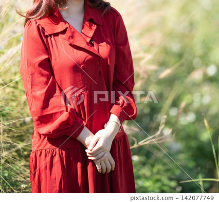 woman wearing a red dress walking through a tall grass field. 142077749