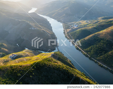 Aerial drone landscape of the Douro River winding through terraced vineyards and steep hills in Portugal's Douro Valley. Aerial drone landscape of the Douro River winding through terraced vineyards and steep hills in Portugal's Douro Valley. 142077866