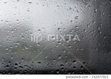 A monochrome background of raindrops and water droplets wetting a windowpane on a stormy or typhoon day. A monochrome background of raindrops and water droplets wetting a windowpane on a stormy or typhoon day. 142077921