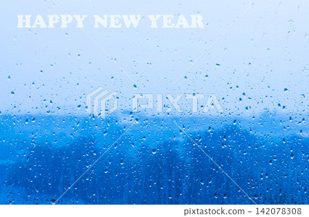 HAPPY NEW YEAR text on rain drops window glass blue background HAPPY NEW YEAR text on rain drops window glass blue background 142078308