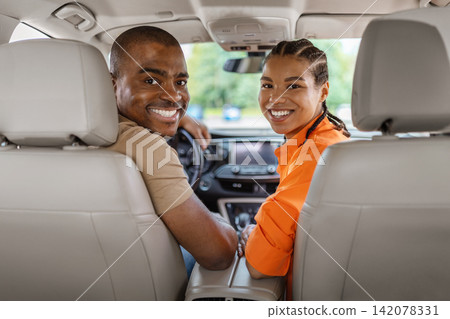 Smiling young Black couple turning toward camera from front seats of car Smiling young Black couple turning toward camera from front seats of car 142078331