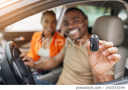Smiling young African American man holding new car key toward camera Smiling young African American man holding new car key toward camera 142078344