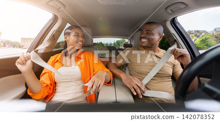 Black couple smiling at each other while fastening seat belts inside car Black couple smiling at each other while fastening seat belts inside car 142078352