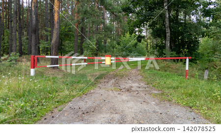 Red-white barrier blocks a forest road. Access restrictions. Barrier in a summer forest. Restricting vehicle access to private property. Red-white barrier blocks a forest road. Access restrictions. Barrier in a summer forest. Restricting vehicle access to private property. 142078525