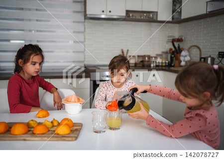 Girls pouring fresh orange juice for breakfast in kitchen Girls pouring fresh orange juice for breakfast in kitchen 142078727