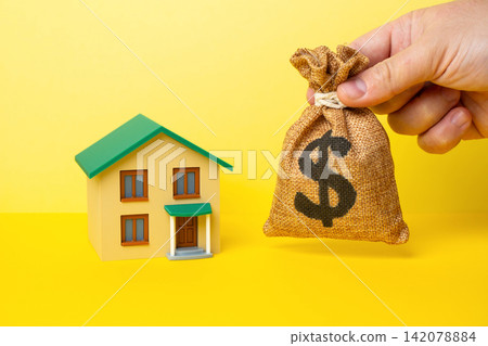 A house and a hand holding a dollar money bag. Buying a house, investing in real estate. Housing market trends. Home renovation loan. A house and a hand holding a dollar money bag. Buying a house, investing in real estate. Housing market trends. Home renovation loan. 142078884
