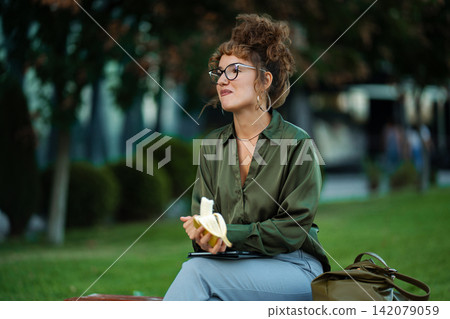 Woman eating banana during outdoor lunch break in park Woman eating banana during outdoor lunch break in park 142079059