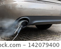 Car exhaust pipe emits dense smoke during emission test on city pavement. Pollution control device measures harmful gases. Service car center garage workshop.  Automobile repair check up diagnosis 142079400