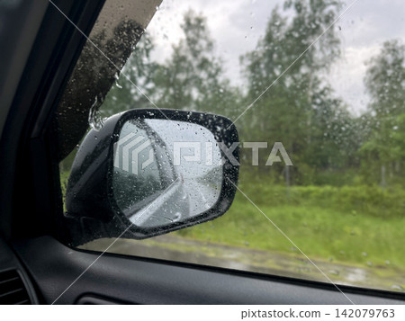 Rainy road trip view through car side mirror with water drops Rainy road trip view through car side mirror with water drops 142079763