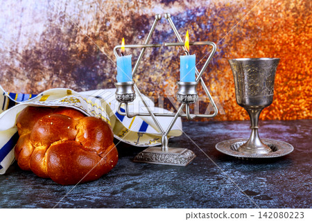Candles in menorah, wine cup, challah bread are set on table for Shabbat celebration at home. Candles in menorah, wine cup, challah bread are set on table for Shabbat celebration at home. 142080223