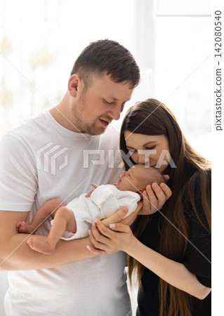 A loving mother kisses her newborn baby while the father holds them both, capturing a tender family moment A loving mother kisses her newborn baby while the father holds them both, capturing a tender family moment 142080540