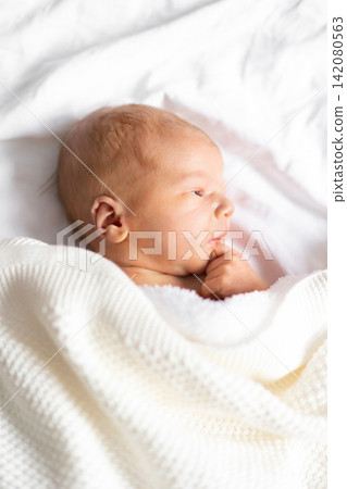 A peaceful newborn baby is swaddled in a soft, textured blanket, resting on clean white sheets A peaceful newborn baby is swaddled in a soft, textured blanket, resting on clean white sheets 142080563