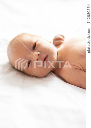 A close-up, soft-focus portrait of a newborn baby with light skin and dark eyes, resting on a white textured surface A close-up, soft-focus portrait of a newborn baby with light skin and dark eyes, resting on a white textured surface 142080584