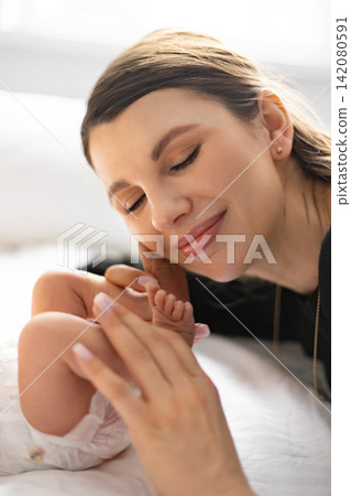 A tender moment captured as a mother gently holds and admires her newborn baby's tiny feet, showcasing the deep bond and love between them 142080591