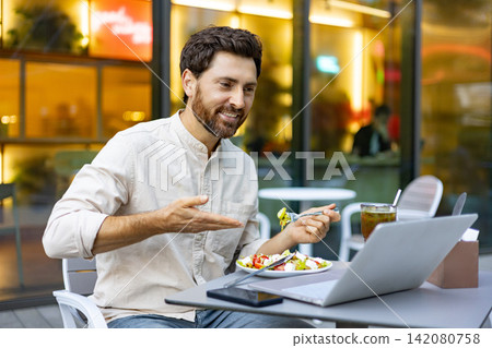A man enjoys a healthy salad and a drink while working on his laptop at an outdoor cafe with a blurred background A man enjoys a healthy salad and a drink while working on his laptop at an outdoor cafe with a blurred background 142080758