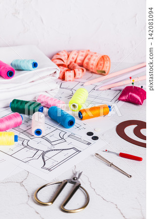 Sewing patterns, threads, scissors, templates and needles on a work table vertical view Sewing patterns, threads, scissors, templates and needles on a work table vertical view 142081094