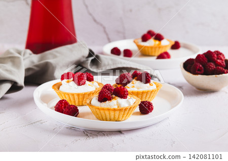 Delicious tartlets with ricotta, jam and raspberries on a plate on the table Delicious tartlets with ricotta, jam and raspberries on a plate on the table 142081101