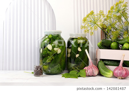 Cucumbers in a basket with dill, garlic, pickling leaves, and pickled cucumbers in jars on a kitchen counter. Harvest concept. Homemade pickle recipe and ingredients. Home canning concept. 142081487