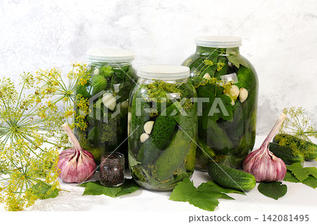 Jarred cucumbers with dill, garlic, and pickling leaves on the kitchen counter. Harvest concept. Homemade pickle recipe and ingredients. Home canning concept. Healthy and natural food. Jarred cucumbers with dill, garlic, and pickling leaves on the kitchen counter. Harvest concept. Homemade pickle recipe and ingredients. Home canning concept. Healthy and natural food. 142081495
