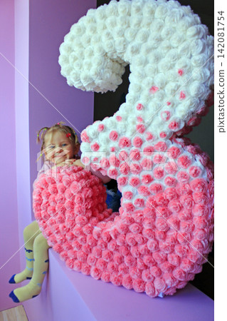 Three years girl sitting near white and pink three made from papier-mache Three years girl sitting near white and pink three made from papier-mache 142081754