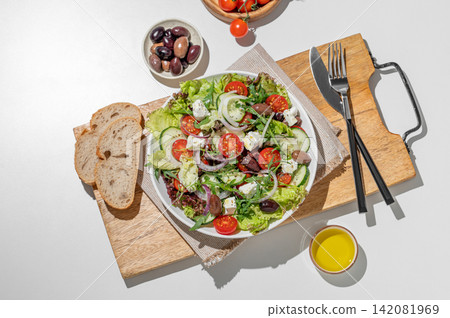 Fresh Greek salad with feta cheese, olives and vegetables in a plate on a white table Fresh Greek salad with feta cheese, olives and vegetables in a plate on a white table 142081969