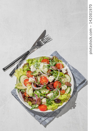 Fresh Greek salad with feta cheese, olives and vegetables in a plate on a light table Fresh Greek salad with feta cheese, olives and vegetables in a plate on a light table 142081970