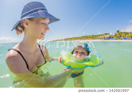 Woman and baby spending time by the Caribbean shore in Mexico, enjoying warm turquoise water, beach vacation, motherhood and travel with baby concept Woman and baby spending time by the Caribbean shore in Mexico, enjoying warm turquoise water, beach vacation, motherhood and travel with baby concept 142081997